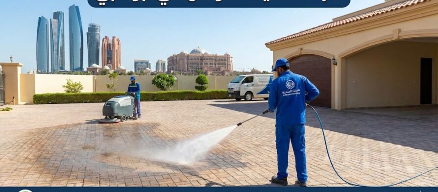 فريق عمل شركة تنظيف احواش في ابوظبي يستخدم معدات غسيل متطورة لتنظيف انترلوك فيلا وإزالة البقع، مع ظهور أبراج أبوظبي في الخلفية