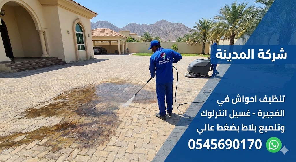 فريق عمل شركة تنظيف احواش في الفجيرة يستخدم ماكينة ضغط عالي وماكينة جلي لتنظيف وإزالة البقع من أرضية انترلوك واسعة في فيلا، مع ظهور جبال الفجيرة في الخلفية.