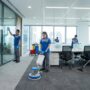فريق عمل متخصص من شركة تنظيف مكاتب في ابوظبي يقوم بمهام تنظيف شاملة داخل مقر إداري حديث، تشمل تلميع الواجهات الزجاجية، جلي الأرضيات، وكنس السجاد باستخدام معدات متطورة.