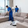 فريق عمل شركة تنظيف مفروشات في الشارقة (شركة المدينة) يقوم بغسيل كنب قماشي باستخدام جهاز البخار في شقة سكنية راقية تطل على أبراج المدينة.