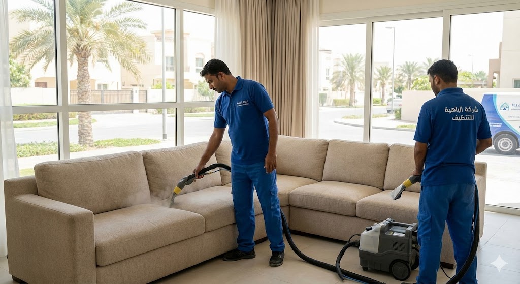 فريق عمل محترف يرتدي زياً أزرق موحد يقوم بعملية غسيل وتنظيف كنب بالبخار لإزالة البقع داخل فيلا سكنية مضيئة، مما يمثل خدمات شركة تنظيف كنب في الباهية.