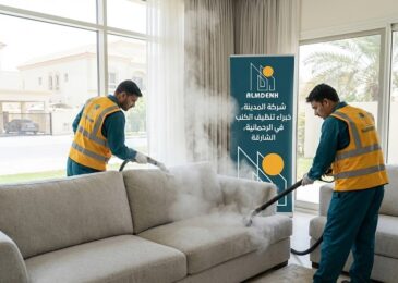 عمال شركة المدينة، بصفتها شركة تنظيف كنب في الرحمانية بالشارقة، يقومون بتنظيف كنب فاتح اللون بالبخار داخل فيلا، مع ظهور لافتة تحمل الهوية البصرية للشركة.