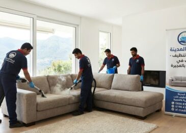 فريق عمل شركة المدينة، بصفتها شركة تنظيف كنب في الشرية، يستخدم أجهزة البخار لتنظيف كنب زاوية كبير في فيلا ذات إطلالة جبلية، مع وجود لافتة إعلانية توضح الخدمة والموقع.