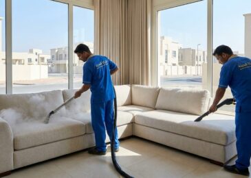 فريق عمل شركة المدينة بزي موحد يقوم بغسيل طقم كنب زاوية بالبخار داخل فيلا حديثة، مما يبرز خدمات أفضل شركة تنظيف كنب في العالية للتعقيم وإزالة البقع.