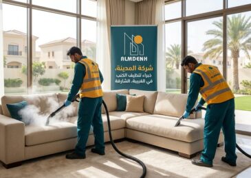 عمال شركة المدينة، بصفتها شركة تنظيف كنب في الغبيبة بالشارقة، يقومون بتنظيف كنب فاتح اللون بالبخار داخل غرفة معيشة مشمسة، مع ظهور لافتة إعلانية تحمل الهوية البصرية للشركة.