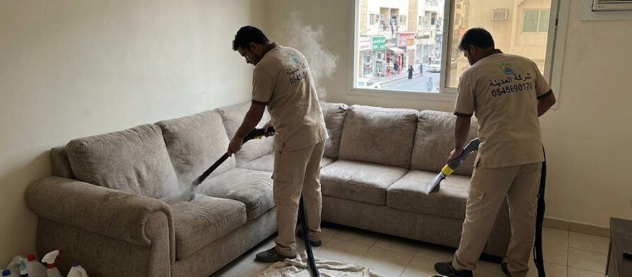 فريق شركة المدينة يقوم بتنظيف كنب بالبخار داخل شقة سكنية تطل على شارع حيوي، موضحاً كفاءة أفضل شركة تنظيف كنب في الكرامة في إزالة الغبار والروائح.