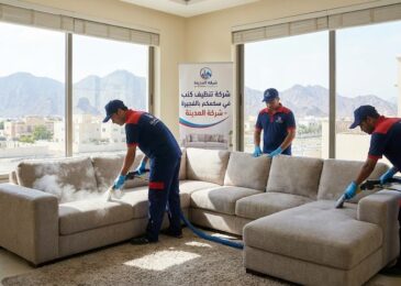 فريق عمل شركة المدينة، بصفتها شركة تنظيف كنب في سكمكم، يستخدم أجهزة البخار لتنظيف كنب كبير في غرفة مطلة على الجبال، مع وجود لافتة توضح الخدمة.