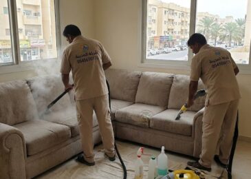 فنيان من شركة المدينة يقومان بتنظيف كنب قماشي بالبخار داخل منزل في حي ليوارة، مما يظهر مهارة أفضل شركة تنظيف كنب في ليوارة في إزالة البقع القديمة.