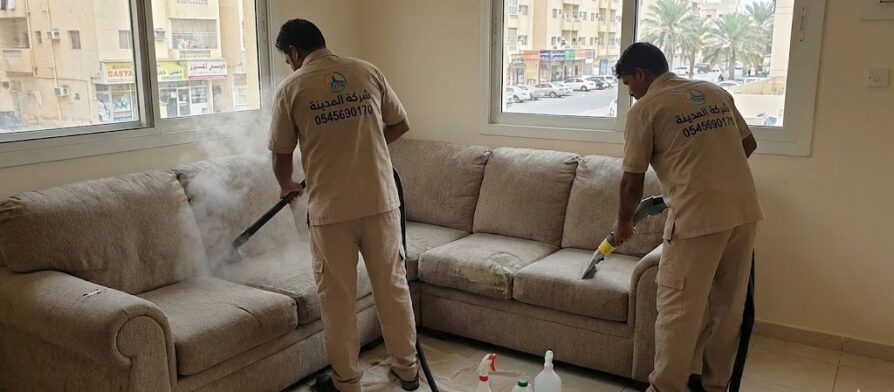 فنيان من شركة المدينة يقومان بتنظيف كنب قماشي بالبخار داخل منزل في حي ليوارة، مما يظهر مهارة أفضل شركة تنظيف كنب في ليوارة في إزالة البقع القديمة.