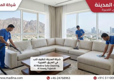 فريق عمل متخصص من شركة المدينة، وهي شركة تنظيف كنب في العريق بالفجيرة، يقوم بعملية تنظيف شاملة لكنب زاوية كبير باستخدام تقنيات البخار والشفط والمسح اليدوي داخل شقة ذات إطلالة جبلية، مع ظهور شعار الشركة ومعلومات الاتصال.