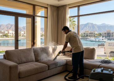 عامل محترف من شركة تنظيف كنب في ميناء العرب ينجز أعمال غسيل وتعقيم أريكة بالبخار داخل منزل ذو إطلالة بحرية.